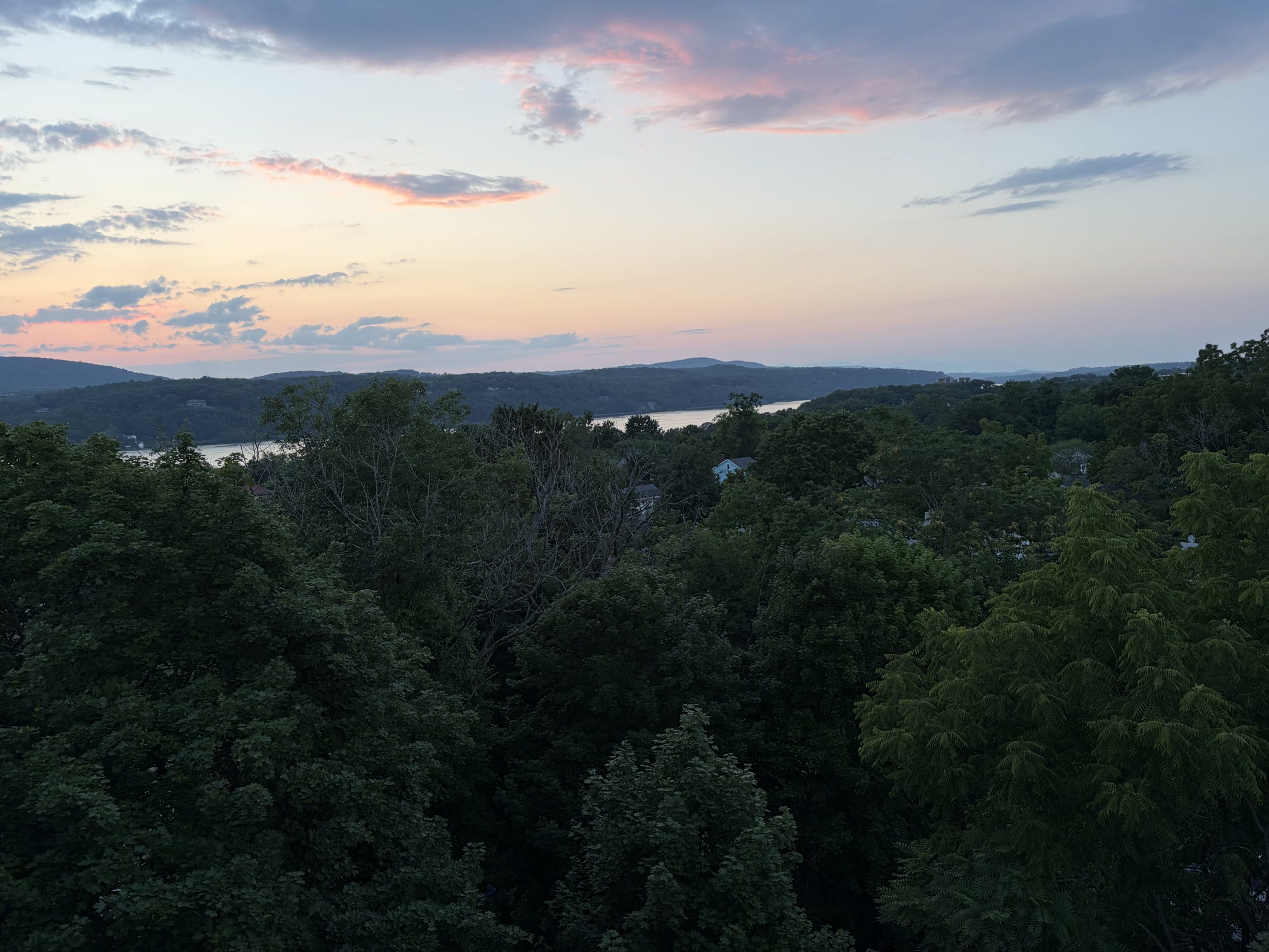 Dusk over the Hudson Valley, pink and orange sky above wooded hills and a bend in the river