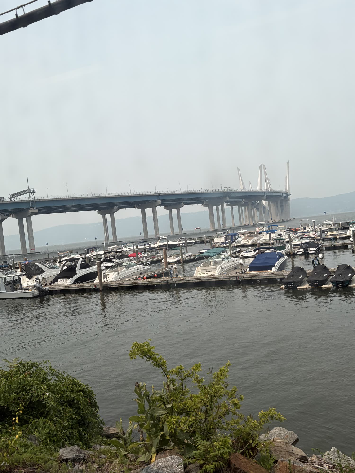 A marina full of boats on the Hudson, a long bridge curving away into the haze behind it, seen from the train into the city