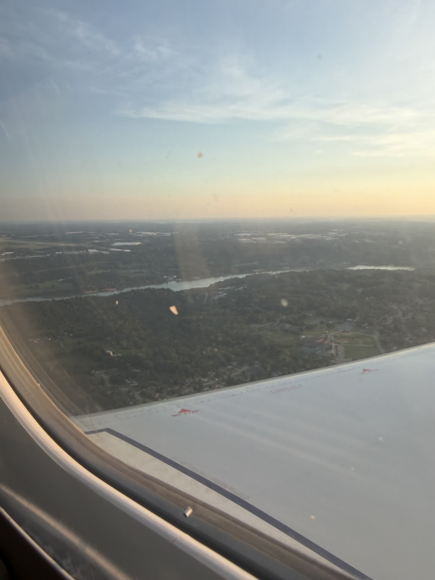Green country and a river out the plane window over the wing, late evening light