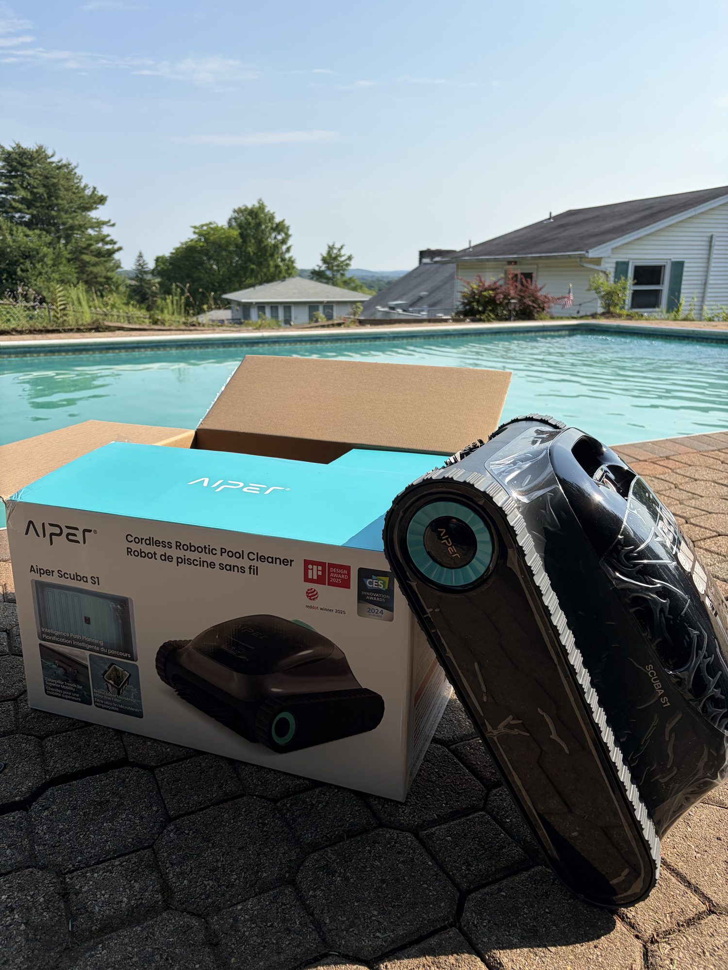 Cordless robotic pool cleaner sitting poolside next to its box